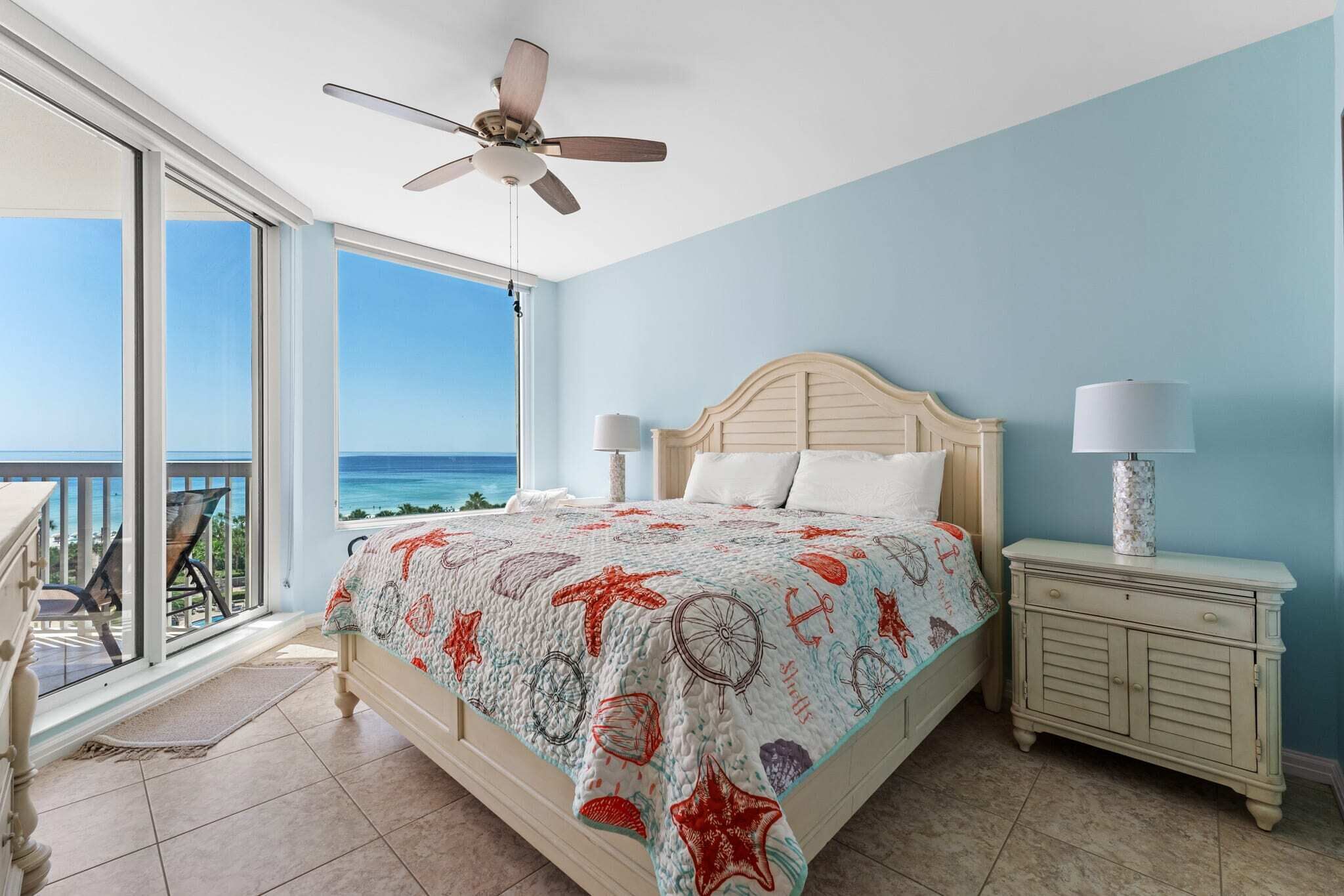 Ein Schlafzimmer mit einem Bett, zwei Nachttischen, einem Deckenventilator und Blick auf das Meer.