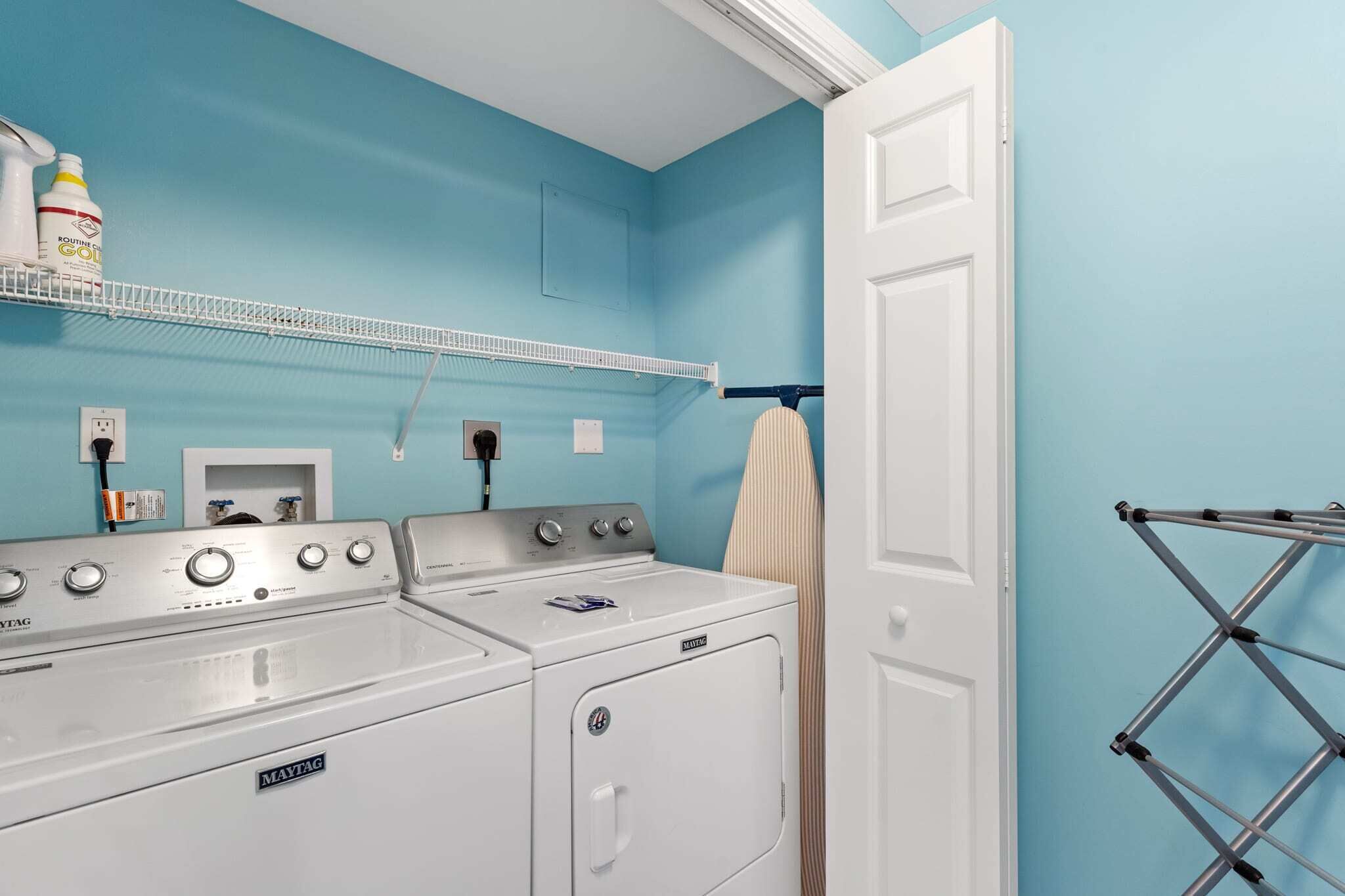 Un área de lavandería con lavadora y secadora Maytag, un estante con productos de limpieza y un tendedero.