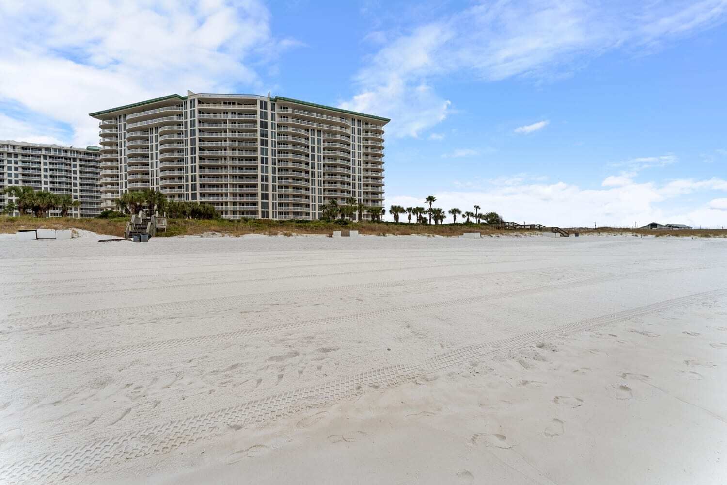 A beachfront hotel with multiple balconies, a sandy beach in the foreground, and palm trees in the background.