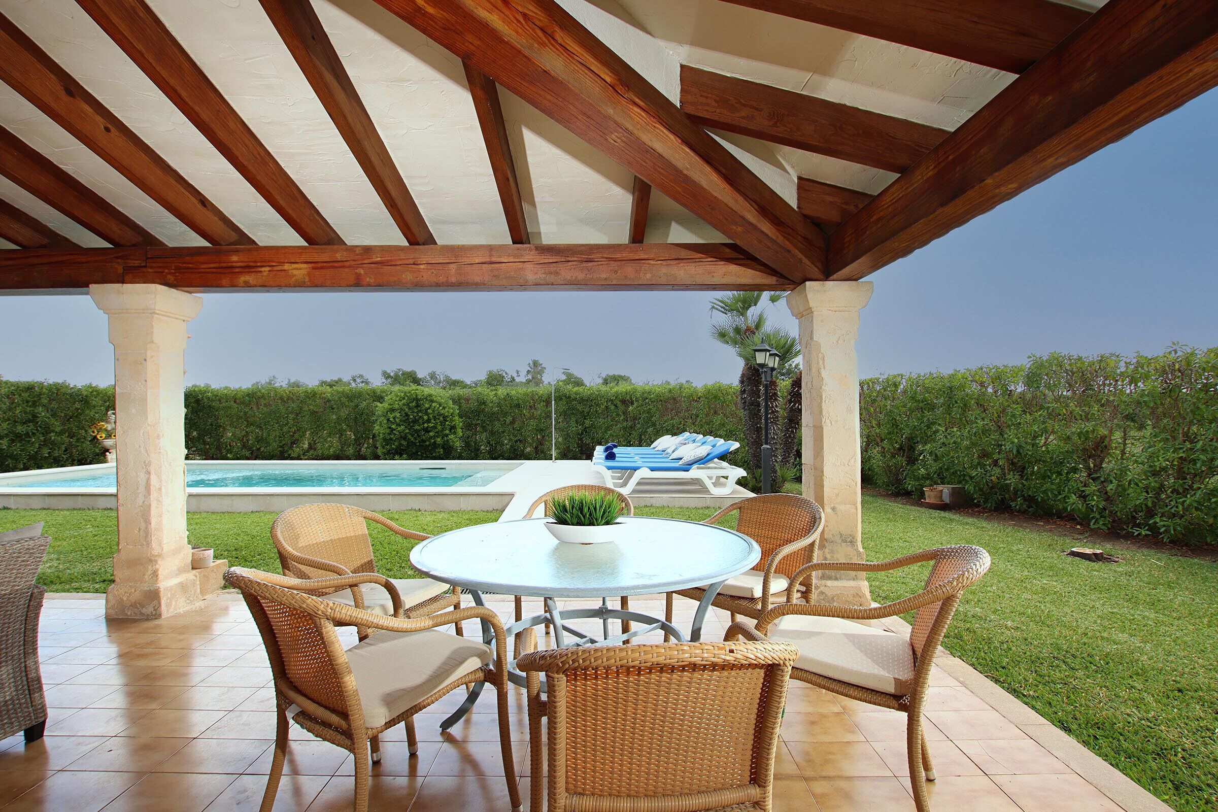 A covered patio with wicker furniture, a round table, and a view of a swimming pool.