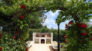 A stone fireplace with a white mantel, surrounded by lush greenery and red flowers. - GERANIOS. Relax and enjoy! (Puerto Pollensa)