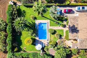 An aerial view of a residential property with a swimming pool, a patio with seating, and a garden with palm trees.