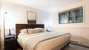 Une chambre à coucher comprenant un lit, des tables de chevet, une commode, une fenêtre avec vue et un tableau accroché au mur.