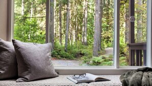Un siège de fenêtre donnant sur une forêt, un livre et une paire de lunettes.