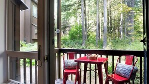 Une terrasse en bois avec une table et deux chaises, donnant sur une zone boisée.