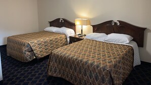 Une chambre d’hôtel avec deux lits, une table de chevet avec une lampe et une moquette à motifs.