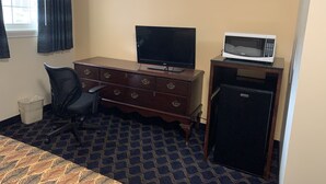 Une chambre d’hôtel comprenant un lit, un bureau avec une télévision, un four à micro-ondes, un réfrigérateur, une chaise et une fenêtre avec des rideaux.