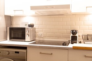 A kitchen with a microwave, toaster, and coffee maker on the counter, a washing machine in the corner, and a white tiled backsplash.