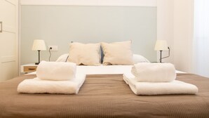 A neatly made bed with two pillows, two bedside lamps, and two folded towels on the bed.