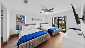 Quarto de hotel moderno com duas camas, um ventilador de teto, uma janela grande com vista e uma televisão de tela plana na parede.