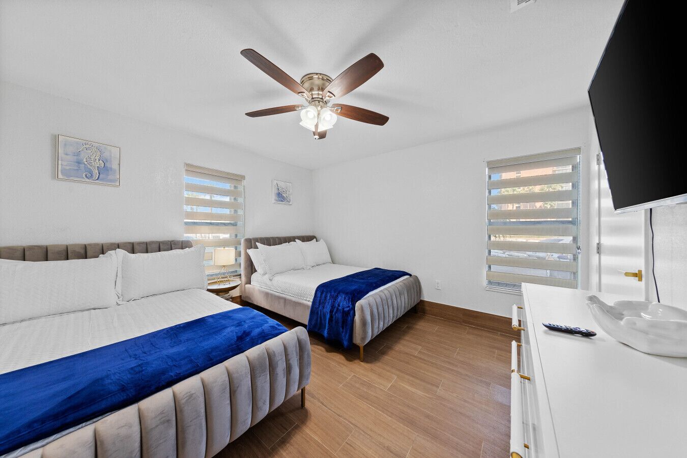 Une chambre d’hôtel avec deux lits, un ventilateur de plafond, une télévision et une fenêtre avec des stores.