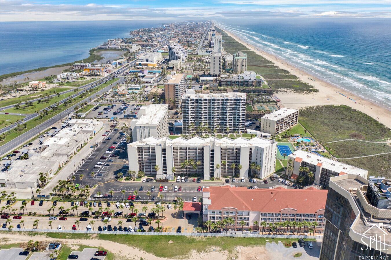Ein Küstenhotel mit mehreren Hochhäusern, einem Parkplatz und Blick auf den Strand.