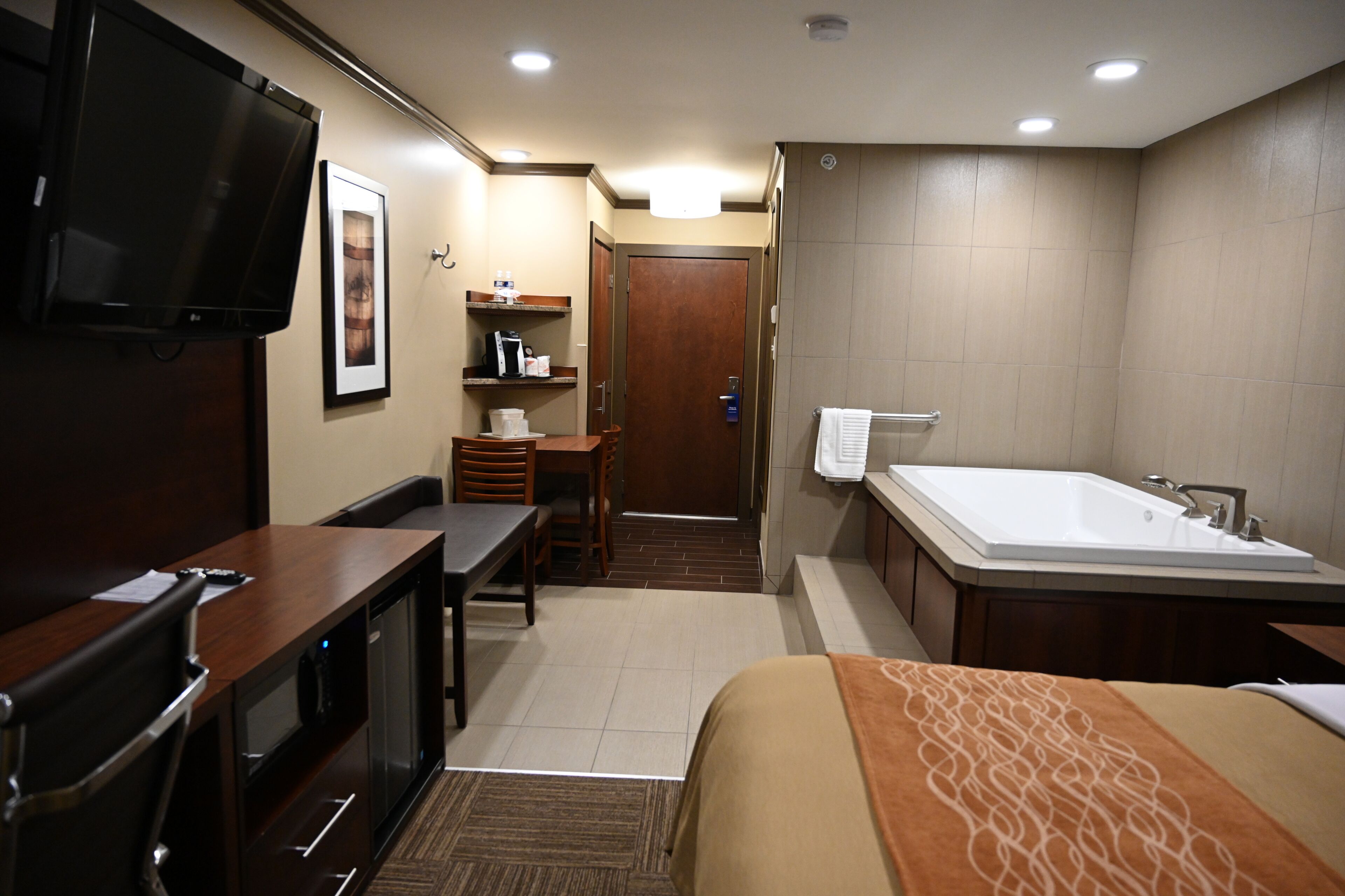 A hotel room with a bed, a desk, a chair, a TV, a bathroom with a bathtub, and a shower.