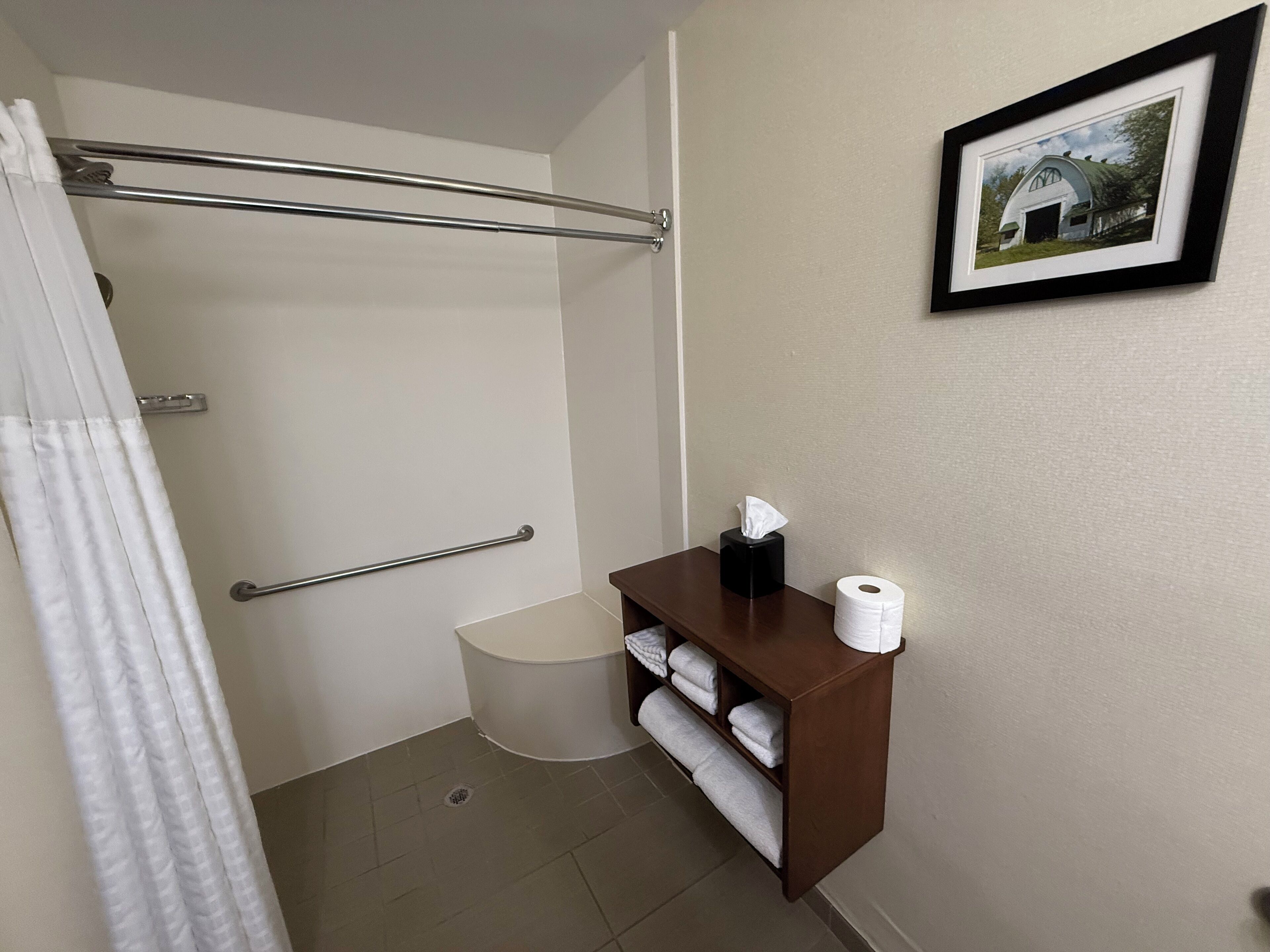 A bathroom with a shower, a toilet, a towel rack, and a shelf with a tissue box and toilet paper.