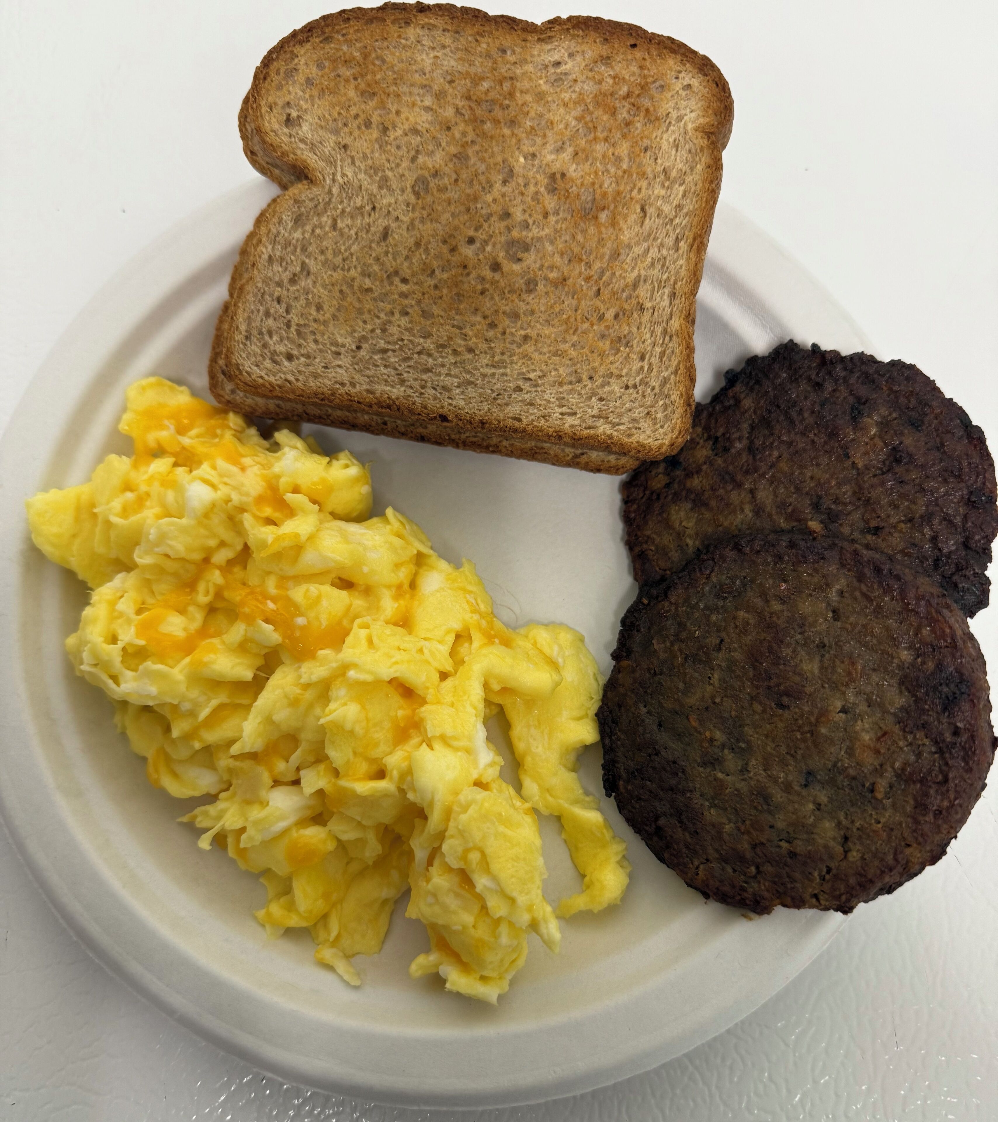 Un plato con huevos revueltos, dos hamburguesas y una rebanada de tostada.