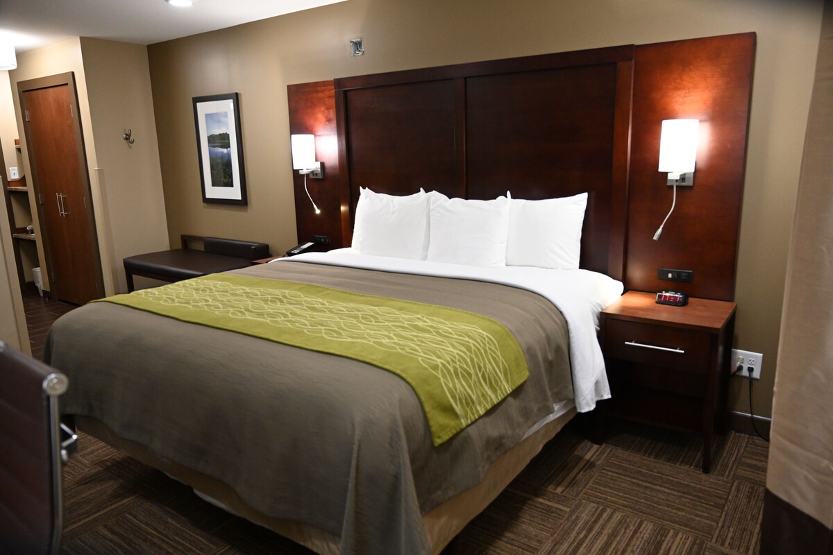 A hotel room with a large bed, a bedside table with a clock, a nightstand with a lamp, and a framed picture on the wall.