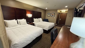 Habitación de hotel con dos camas, un escritorio, una silla, una mesita de noche, una lámpara y una puerta.