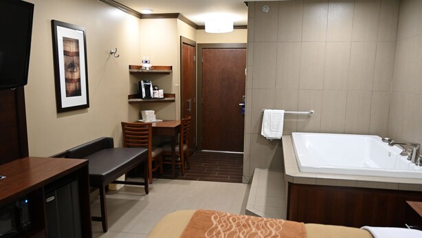 Une chambre d’hôtel comprenant un lit, un bureau, une chaise, une petite table, une télévision, une salle de bain avec baignoire et une douche.