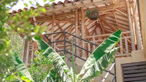 Une structure en bambou surmontée d’un toit en tuiles, avec un escalier en métal et un pot de fleurs suspendu.