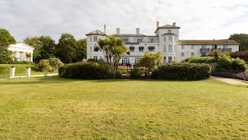 A large, white, multi-story building with a symmetrical facade, surrounded by well-maintained lawns and mature trees.
