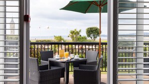 A balcony with wicker chairs and a table set for breakfast, overlooking a scenic view with a clock tower and palm trees. - The Imperial Hotel (Exmouth)