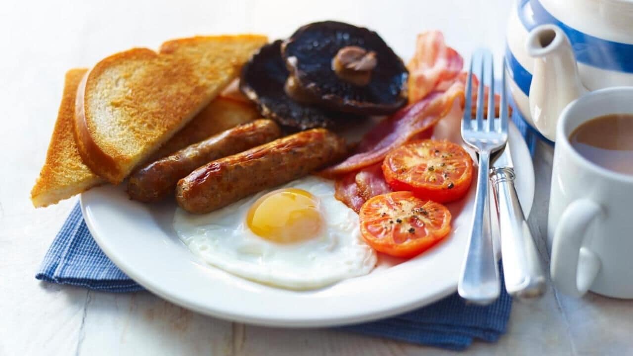 Une assiette avec des toasts, des saucisses, du bacon, un œuf au plat et des tomates.
