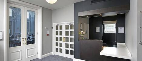 Un área de recepción con un mostrador oscuro, un mostrador blanco y una puerta de cristal que da a una sala de espera.