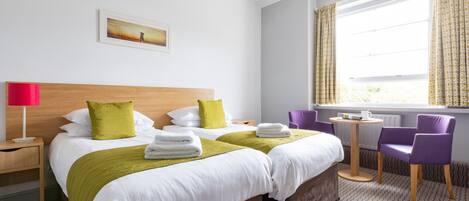 Una habitación de hotel con una cama grande, una mesita de noche, una silla, una pequeña mesa y una ventana con cortinas.