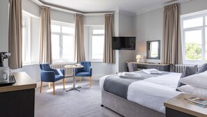 A hotel room with a large bed, a desk, a chair, a TV, and a window with curtains. - The Imperial Hotel (Exmouth)