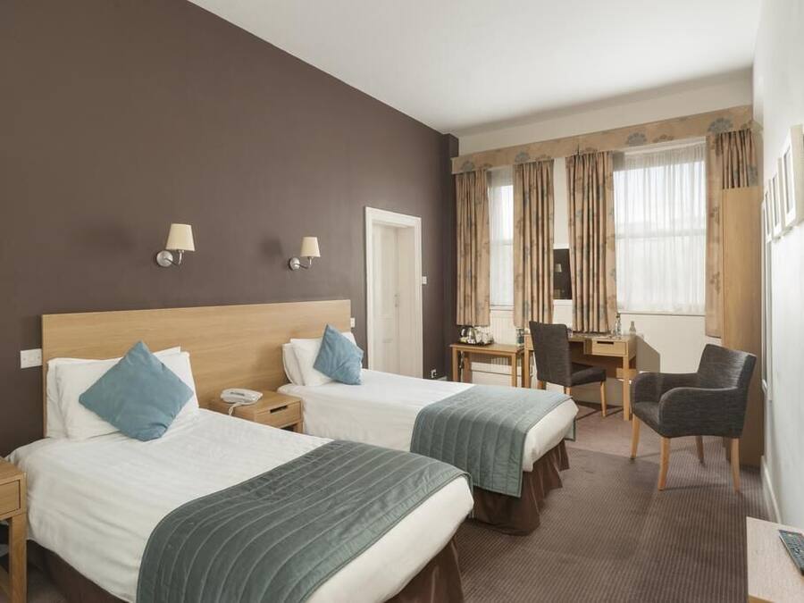A hotel room with two beds, a desk, a chair, a TV, and a phone on the nightstand.