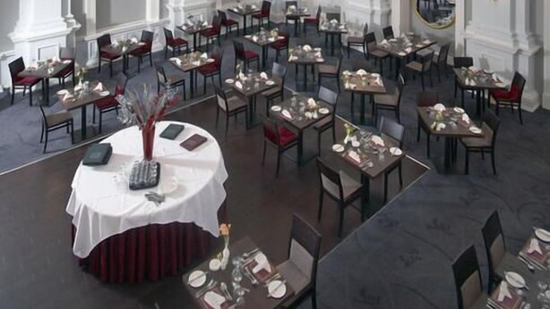 A formal dining room with multiple tables and chairs, white columns, and a chandelier. - The Imperial Hotel (Exmouth)