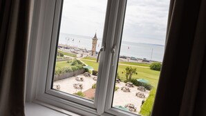 A view through a window of a coastal area with a clock tower, outdoor seating, and a grassy lawn. - The Imperial Hotel (Exmouth)