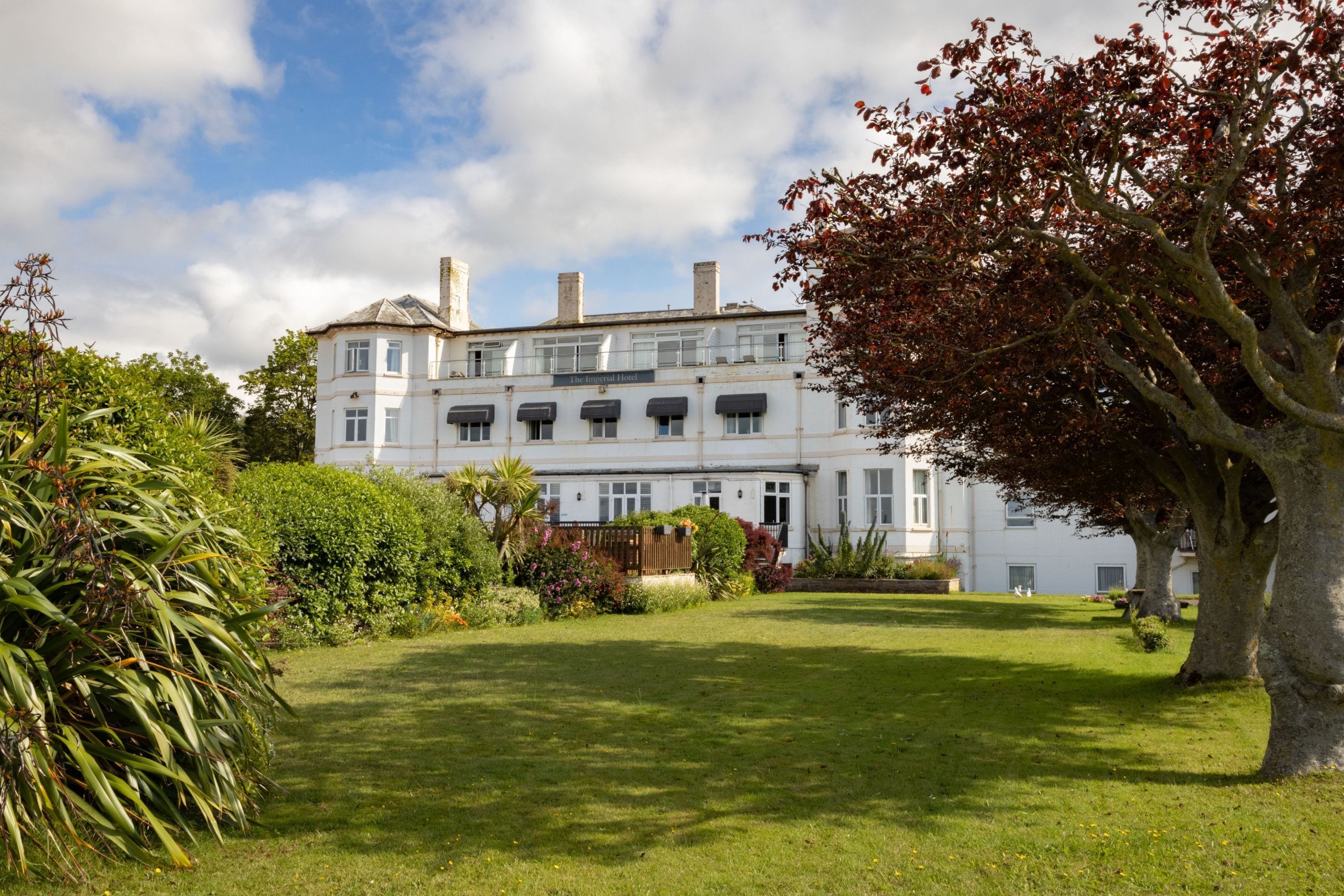 A large, white building with multiple windows and a well-maintained garden.