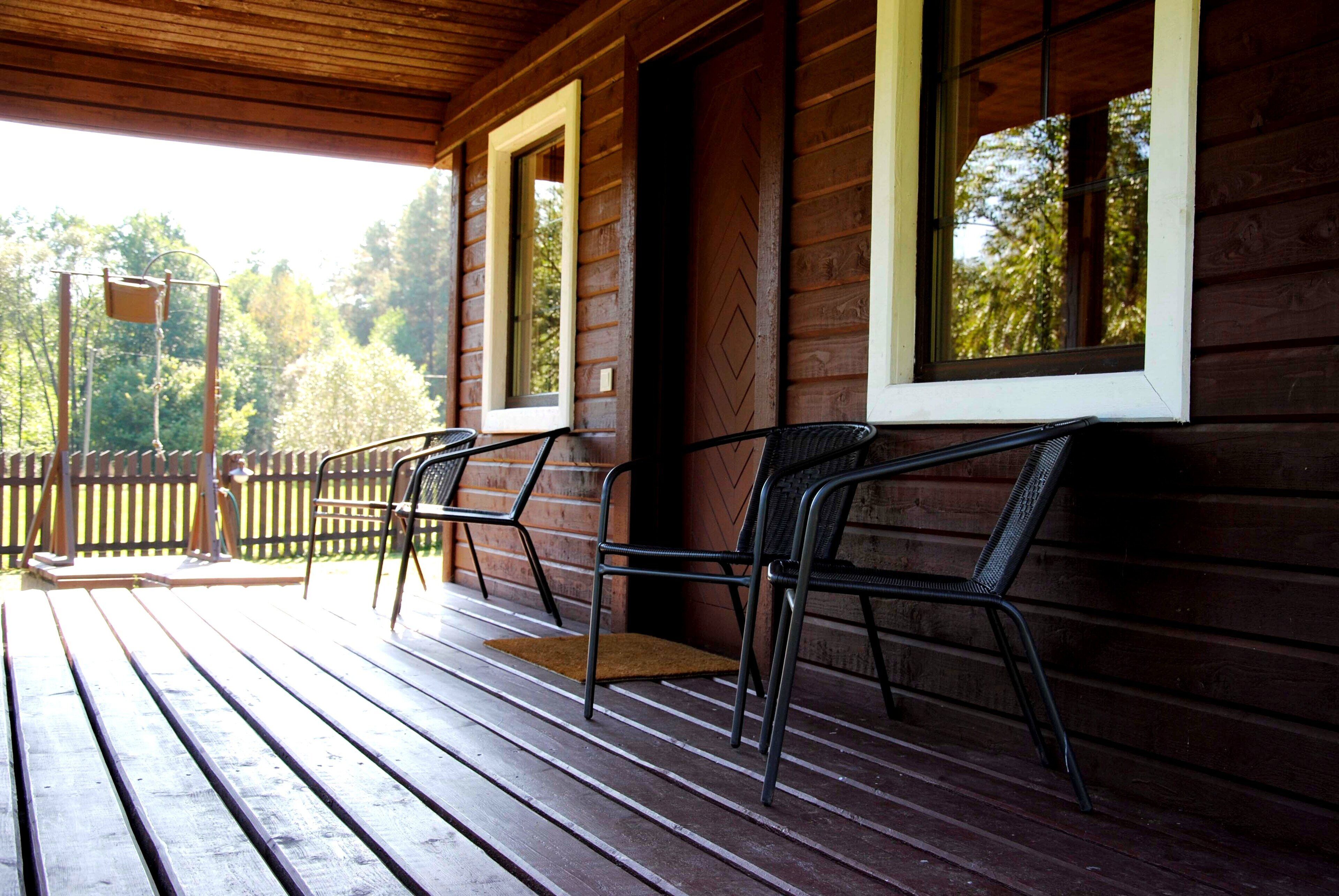 A wooden porch with two metal chairs and a wooden bench.