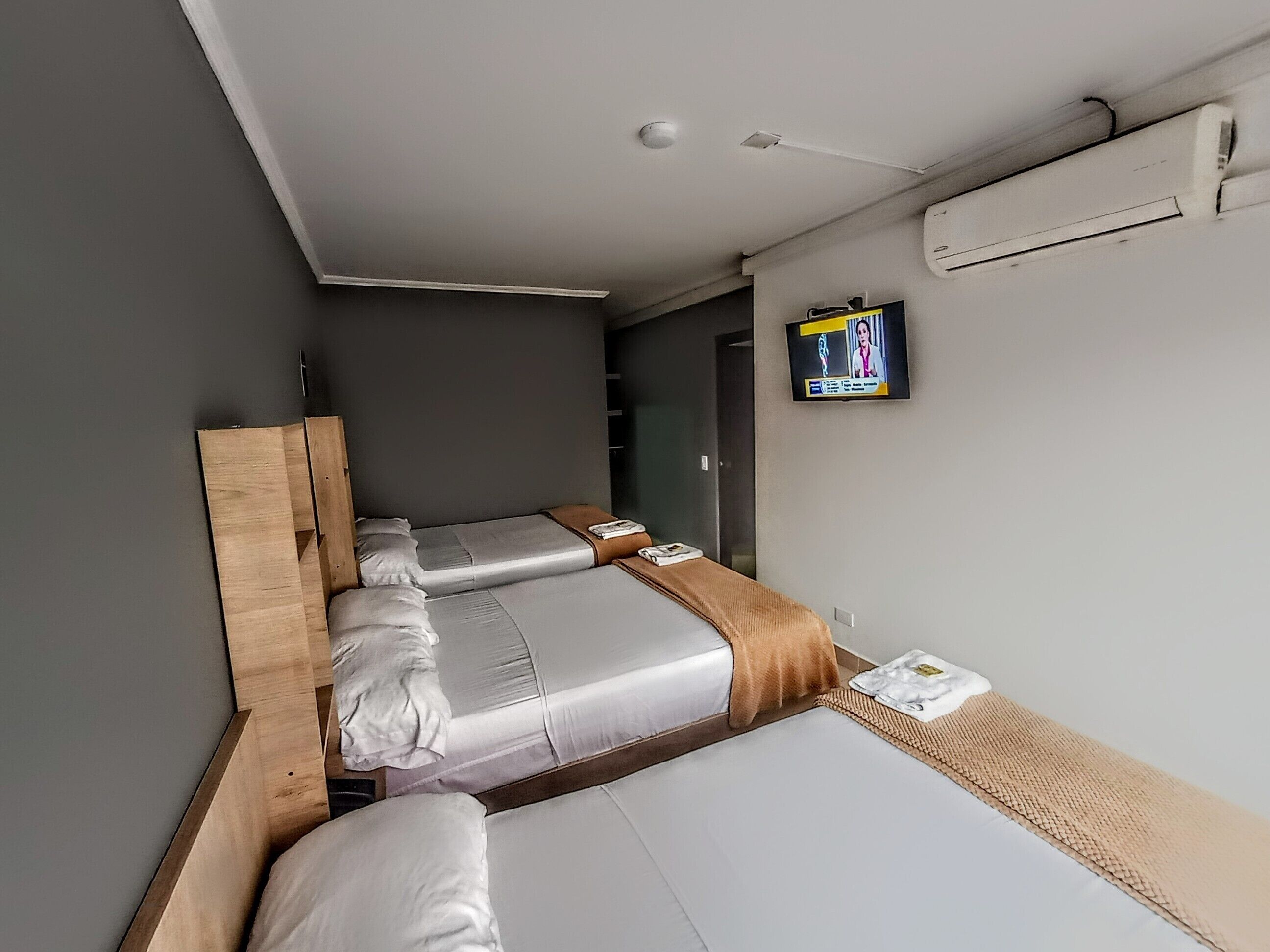 A hotel room with two beds, a TV on the wall, and an air conditioning unit.