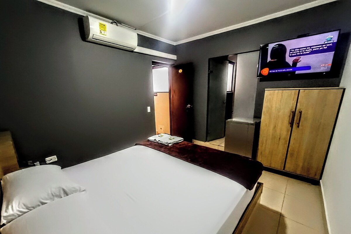 A hotel room with a bed, a television, a wardrobe, and an air conditioning unit.