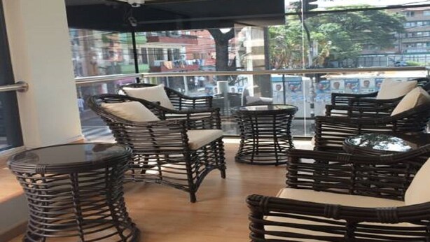 A balcony with wicker furniture and glass tables, overlooking a cityscape. - Hotel Ruiseñor  (Itagüí)