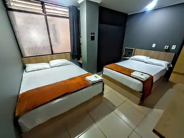 Une chambre d’hôtel avec deux lits, une fenêtre avec des stores, une petite table et une table de chevet.