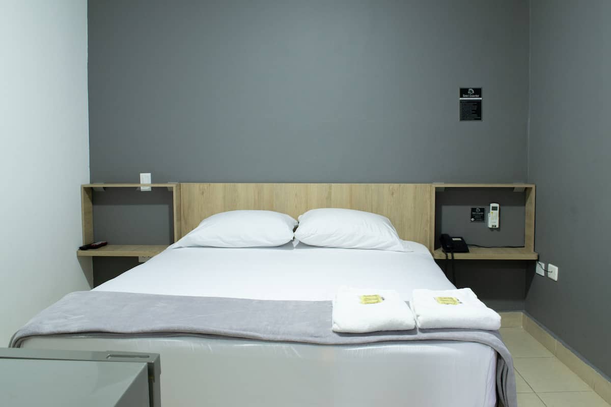 Une chambre d’hôtel avec un lit, deux oreillers, une table de chevet avec un téléphone et une petite étagère.