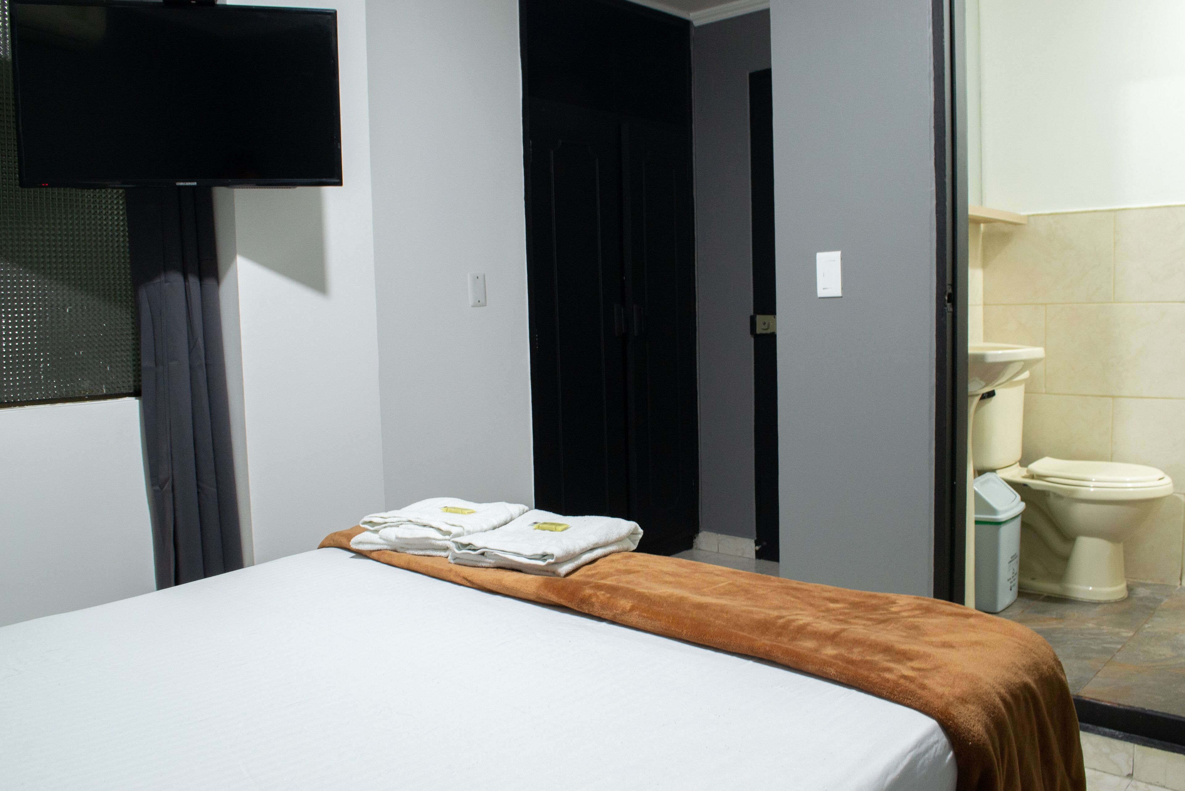 A hotel room with a bed, a TV mounted on the wall, and a bathroom with a toilet and sink.