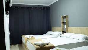 A hotel room with two beds, dark curtains, a wooden shelf, and a white wall. - Hotel Ruiseñor  (Itagüí)