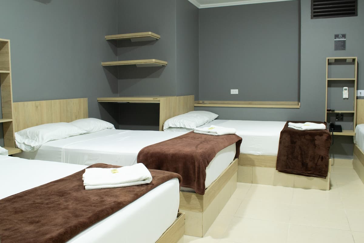 Une chambre d’hôtel avec trois lits, des têtes de lit en bois et des étagères intégrées.