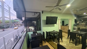 A restaurant with a view of a street, tables and chairs, a ceiling fan, and a TV mounted on the wall. - Hotel Ruiseñor  (Itagüí)