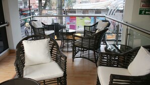 A balcony with wicker furniture and a glass railing. - Hotel Ruiseñor  (Itagüí)