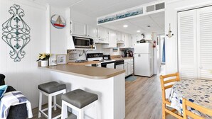 A compact kitchen with white cabinets, a central island with stools, a microwave, stove, and refrigerator. - Seven Seas - Recently Remodeled Ocean Block 1 Bedroom! (Ocean City)