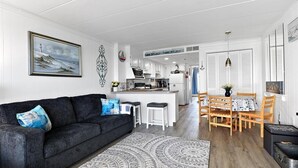 A modern living room with a dark sofa, a patterned rug, and a dining area with wooden chairs and a table. - Seven Seas - Recently Remodeled Ocean Block 1 Bedroom! (Ocean City)