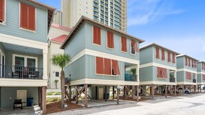 Een rij strandbungalows met verhoogde constructies, buitenzitplaatsen en een palmboom.