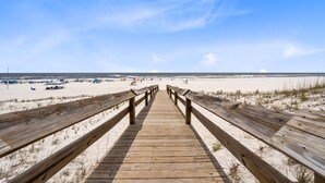 Een houten looppad dat naar een zandstrand leidt, met parasols en mensen op het strand.