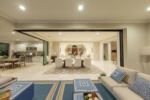 Relax in this open-plan living space with a central dining area, featuring a sofa, armchair, and kitchen with modern appliances.