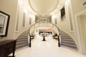 Stunning staircase leads to an upper level, flanked by large windows and surrounded by elegant artwork and seating.